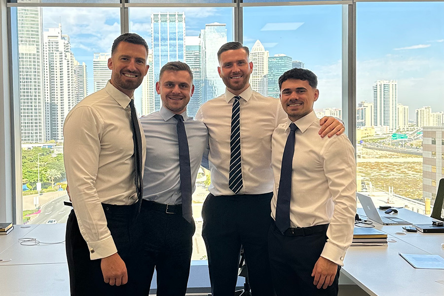four harris and co team members smiling in front of window with dubai cityscape in background