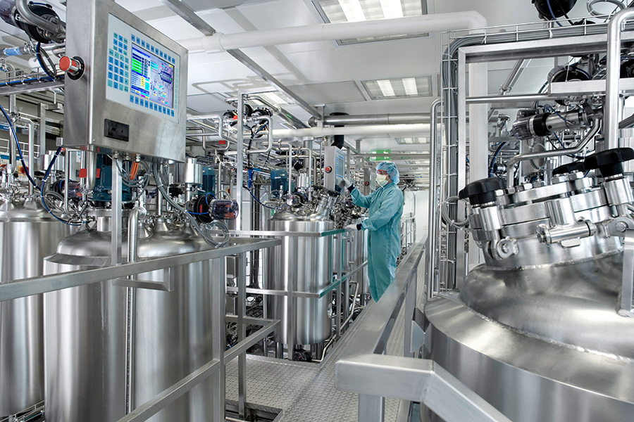 inside a science lab with steel tanks, and scientist in biohazard gear in the background