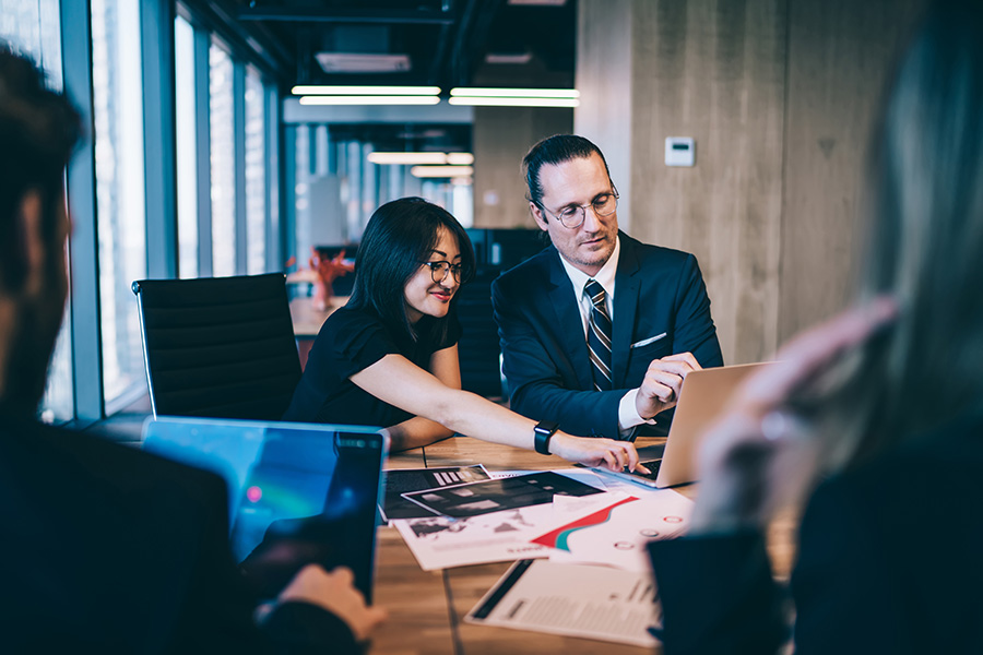 executives around a desk with woman pointing to laptop screen