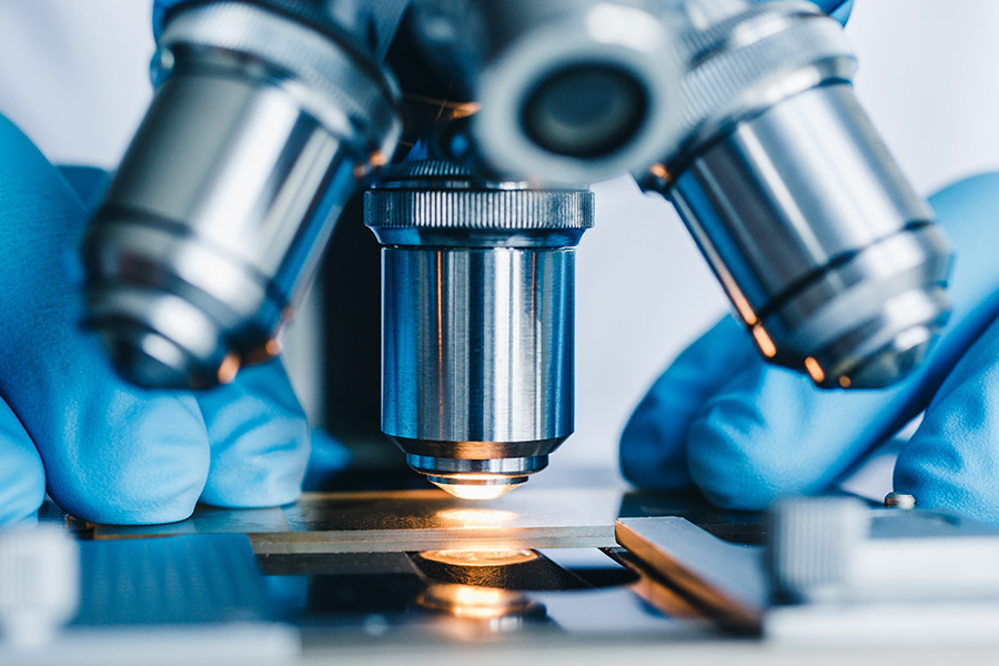 A microscope focuses on a slide, illuminated from below, while blue-gloved hands adjust its settings in a laboratory environment.