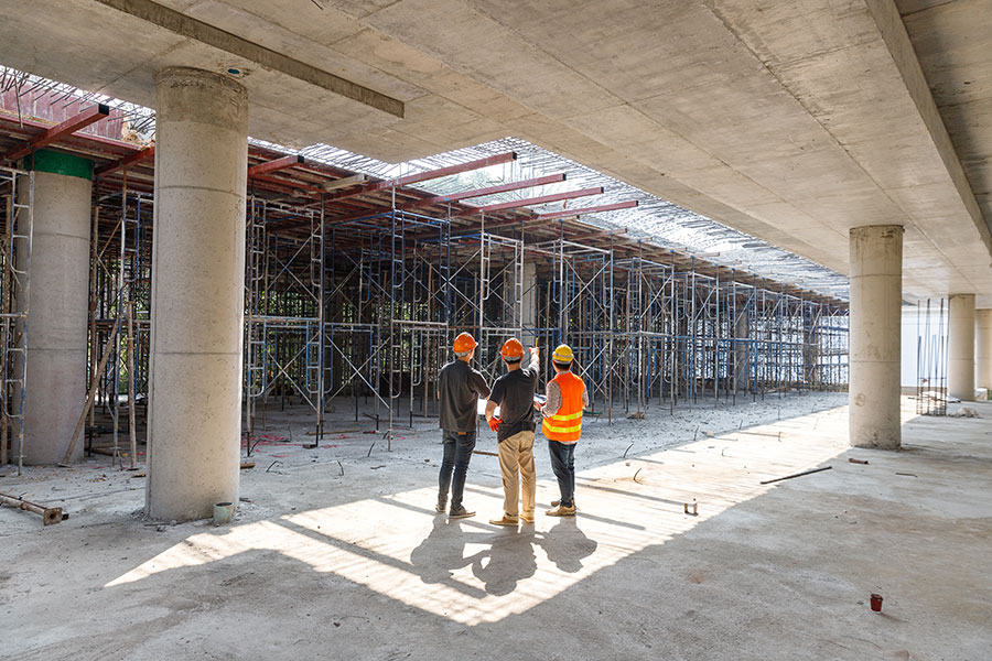 3 construction workers on job site with scaffolding and one pointing at the work